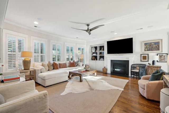 living area with wood finished floors, visible vents, a fireplace with flush hearth, ceiling fan, and crown molding