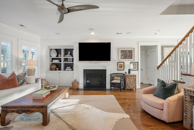 living area with visible vents, ceiling fan, a fireplace with flush hearth, stairs, and wood finished floors