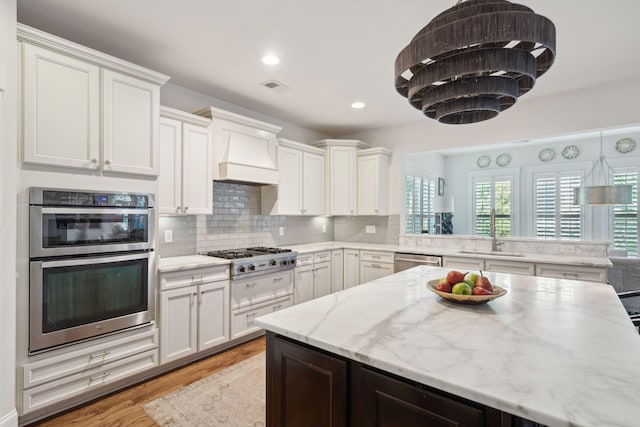 kitchen with visible vents, custom range hood, a sink, tasteful backsplash, and stainless steel appliances