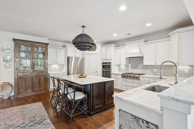 kitchen with a sink, light stone counters, appliances with stainless steel finishes, and custom range hood