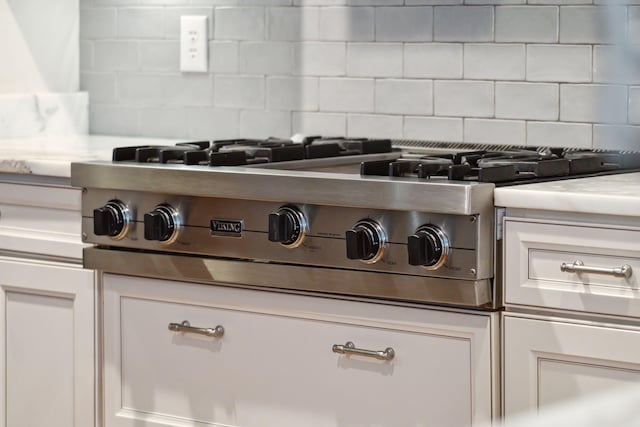 room details featuring decorative backsplash, white cabinetry, and stainless steel gas cooktop