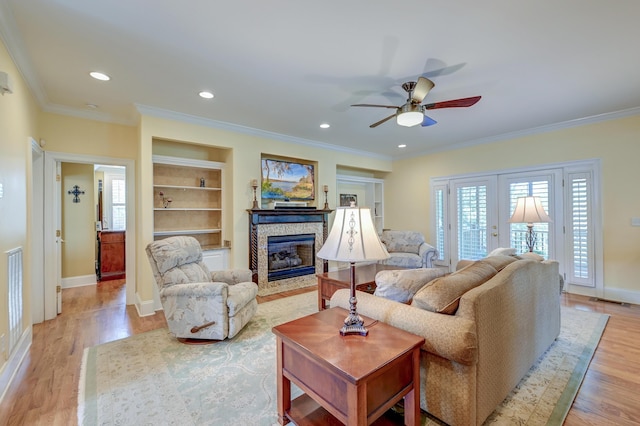 living room with a stone fireplace, light hardwood / wood-style flooring, ornamental molding, built in shelves, and french doors