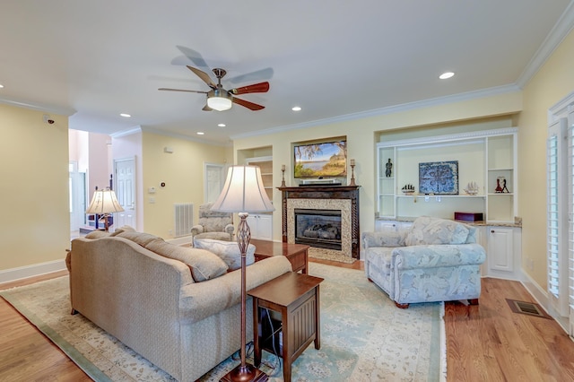 living room with built in shelves, ceiling fan, ornamental molding, and light wood-type flooring