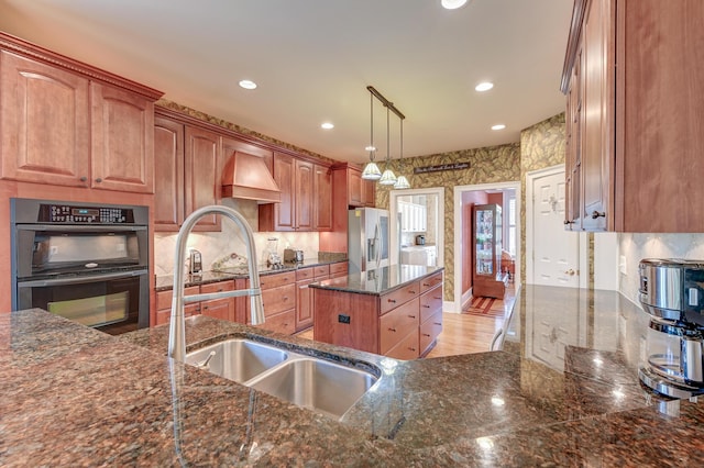 kitchen featuring sink, a center island, stainless steel fridge with ice dispenser, hanging light fixtures, and double wall oven