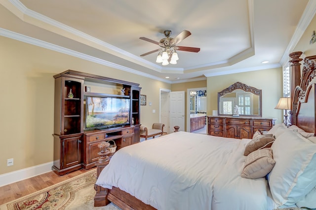 bedroom featuring connected bathroom, crown molding, light hardwood / wood-style flooring, a tray ceiling, and ceiling fan