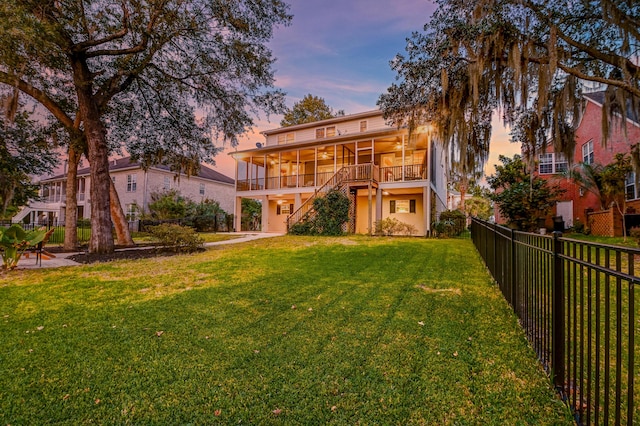 back house at dusk with a yard and a sunroom