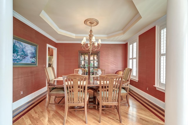 dining area with a raised ceiling, a chandelier, and light hardwood / wood-style flooring