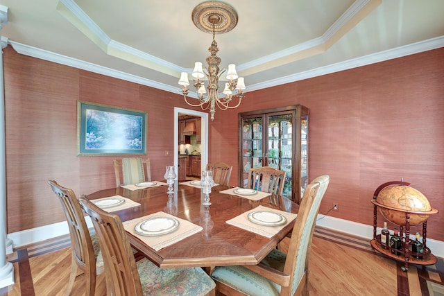 dining room featuring a notable chandelier, a tray ceiling, ornamental molding, and light wood-type flooring