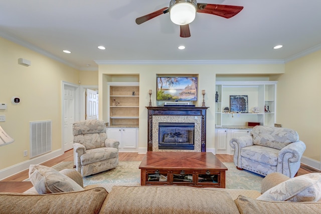 living room with built in features, ornamental molding, ceiling fan, and light wood-type flooring