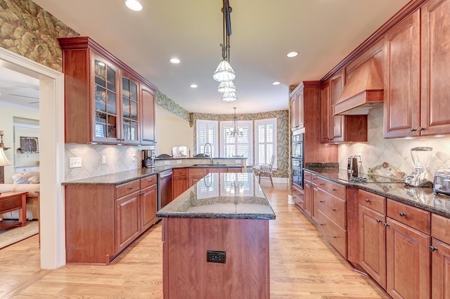 kitchen featuring premium range hood, sink, decorative light fixtures, a center island, and dark stone counters