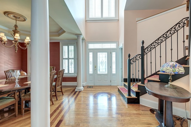 foyer entrance with crown molding, a chandelier, light wood-type flooring, and ornate columns