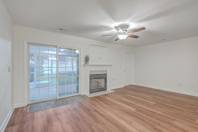 unfurnished living room featuring ceiling fan, a tiled fireplace, and light wood-type flooring