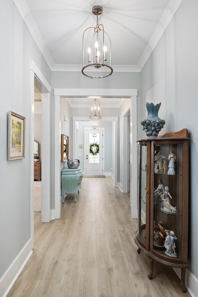 hall featuring an inviting chandelier, ornamental molding, and light wood-type flooring