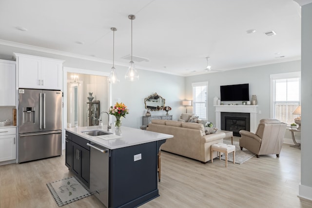 kitchen featuring pendant lighting, sink, appliances with stainless steel finishes, white cabinets, and a center island with sink