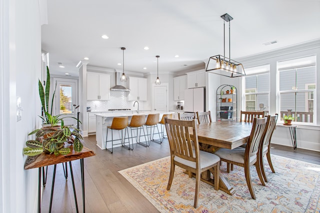 dining room featuring crown molding, light wood finished floors, recessed lighting, visible vents, and baseboards