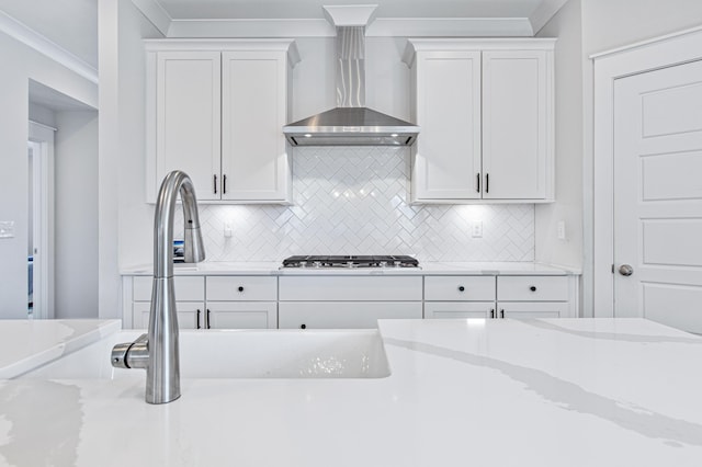 kitchen with ornamental molding, white cabinets, wall chimney range hood, and gas cooktop