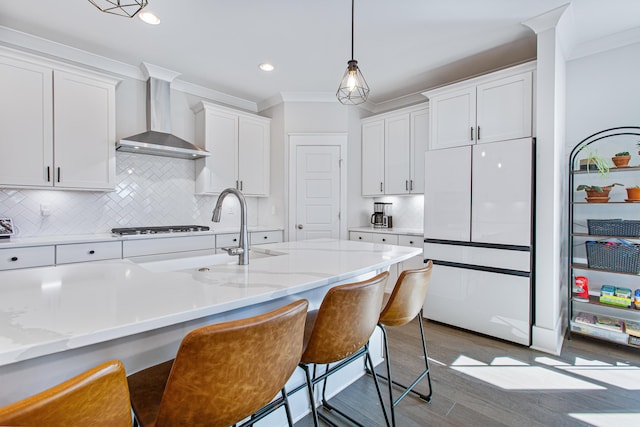 kitchen with crown molding, gas stovetop, white cabinets, wall chimney exhaust hood, and white refrigerator