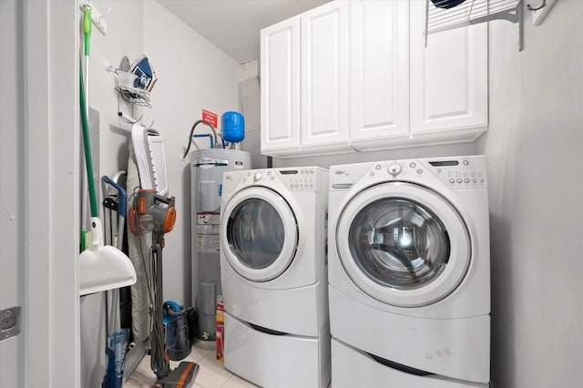 laundry area with electric water heater, washing machine and dryer, cabinet space, and light tile patterned flooring