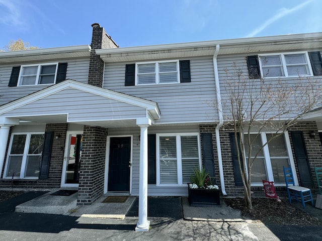 townhome / multi-family property with brick siding, covered porch, and a chimney