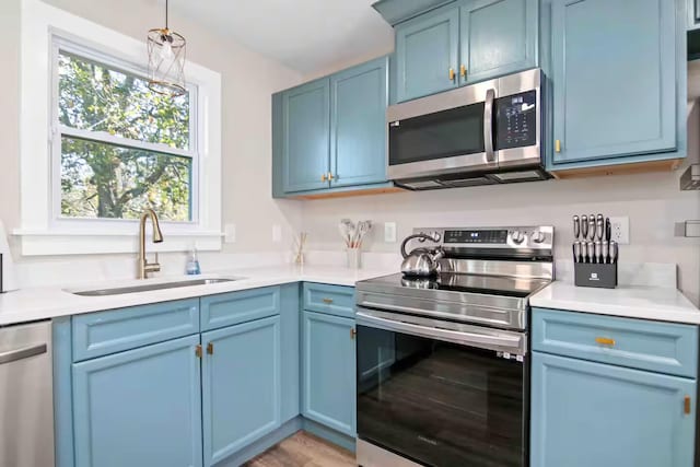 kitchen with blue cabinets, sink, pendant lighting, and appliances with stainless steel finishes