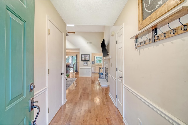 foyer featuring light wood-type flooring, a textured ceiling, and a fireplace with raised hearth