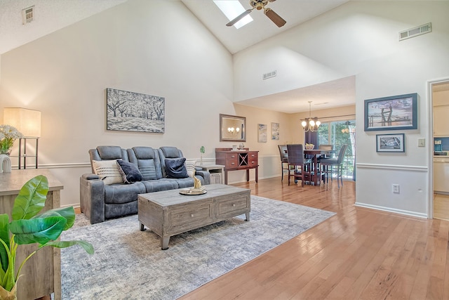 living room featuring high vaulted ceiling, light wood finished floors, a chandelier, ceiling fan, and baseboards