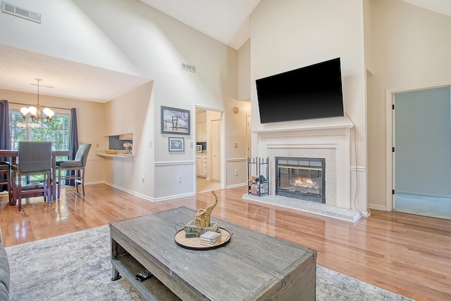 living area featuring a chandelier, wood finished floors, high vaulted ceiling, baseboards, and a brick fireplace