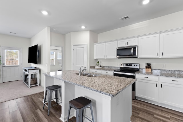 kitchen featuring appliances with stainless steel finishes, white cabinetry, an island with sink, sink, and light stone counters