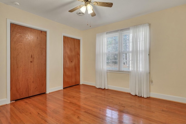 unfurnished bedroom featuring ceiling fan, light hardwood / wood-style flooring, and multiple closets