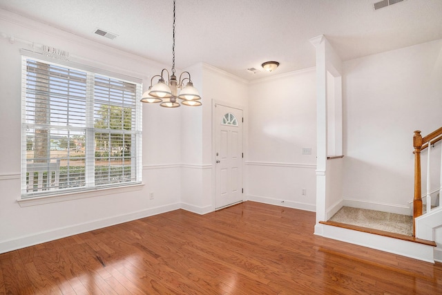 unfurnished dining area featuring crown molding, hardwood / wood-style floors, a textured ceiling, and a notable chandelier