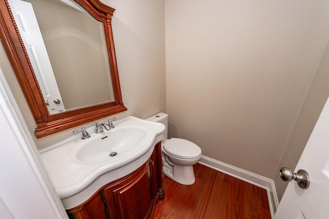 half bath with vanity, baseboards, toilet, and wood finished floors