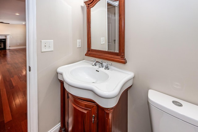 half bathroom with a fireplace, toilet, wood finished floors, and vanity