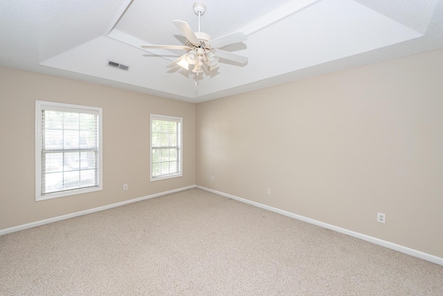 empty room featuring a ceiling fan, light colored carpet, visible vents, a raised ceiling, and baseboards