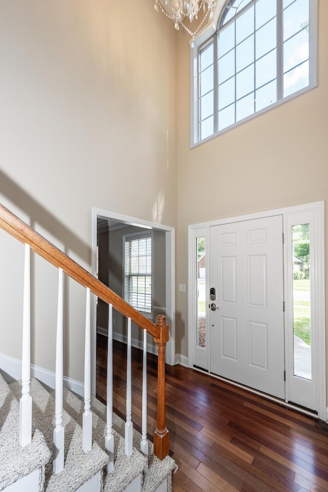 entryway featuring wood-type flooring, an inviting chandelier, a towering ceiling, stairway, and plenty of natural light
