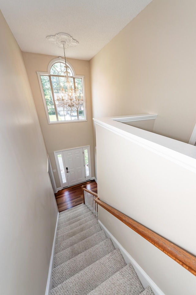 staircase featuring a textured ceiling, baseboards, an inviting chandelier, and wood finished floors