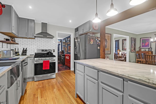 kitchen featuring tasteful backsplash, decorative light fixtures, gray cabinets, appliances with stainless steel finishes, and wall chimney exhaust hood