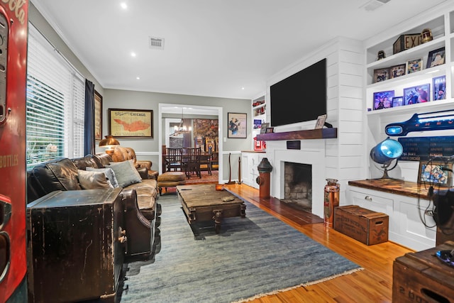 living room featuring a fireplace, a notable chandelier, hardwood / wood-style floors, crown molding, and built in shelves