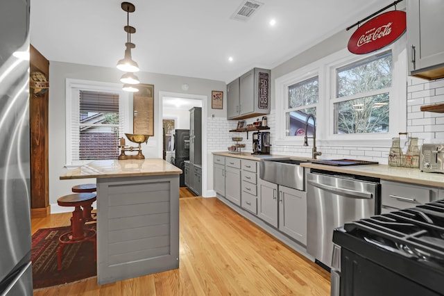 kitchen featuring appliances with stainless steel finishes, decorative light fixtures, sink, backsplash, and gray cabinetry