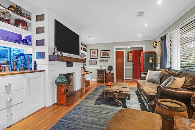 living room featuring built in features, ornamental molding, and light hardwood / wood-style flooring