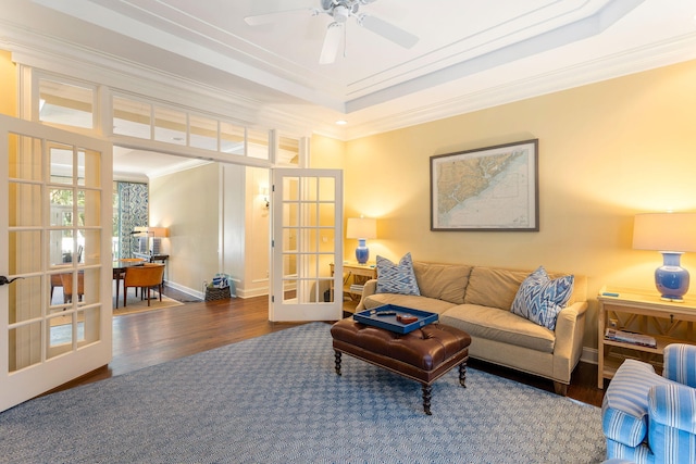 living room featuring dark wood-type flooring, a raised ceiling, ornamental molding, ceiling fan, and french doors