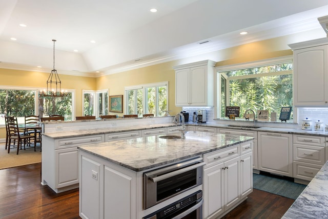 kitchen with a kitchen island with sink, white cabinets, kitchen peninsula, hanging light fixtures, and decorative backsplash