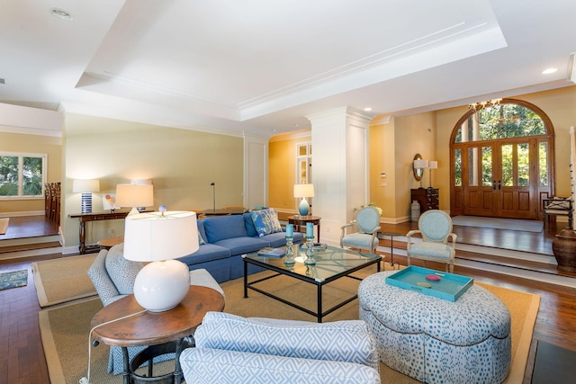 living room featuring wood-type flooring, a chandelier, decorative columns, and a raised ceiling