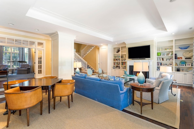 living room with wood-type flooring, built in shelves, crown molding, and a raised ceiling