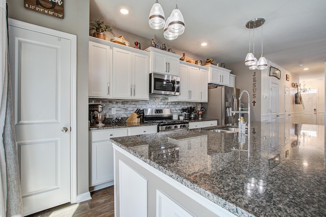 kitchen featuring a kitchen island with sink, a sink, backsplash, white cabinetry, and stainless steel appliances