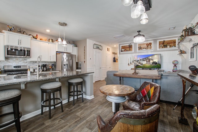 kitchen featuring backsplash, dark wood finished floors, a breakfast bar, dark stone counters, and appliances with stainless steel finishes