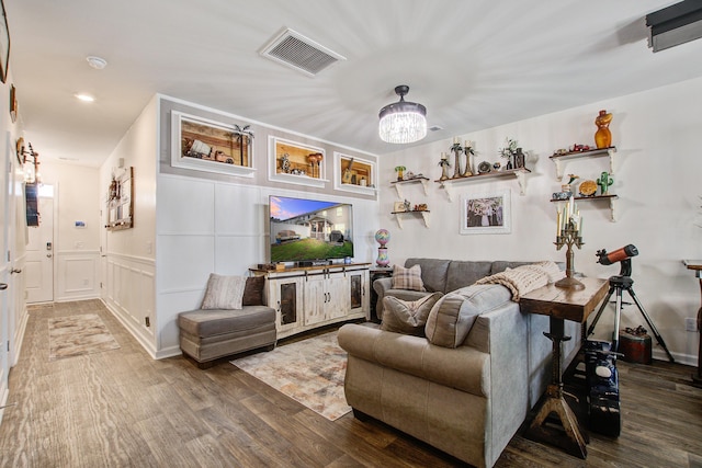 living area with visible vents, a chandelier, a wainscoted wall, wood finished floors, and a decorative wall