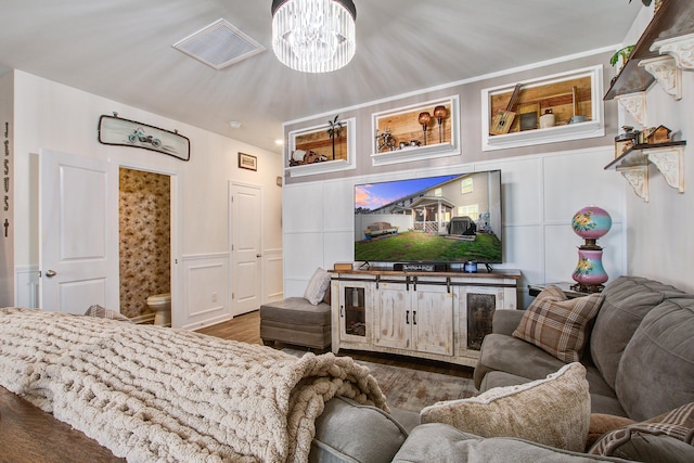 living area with wood finished floors, a wainscoted wall, visible vents, a decorative wall, and a chandelier