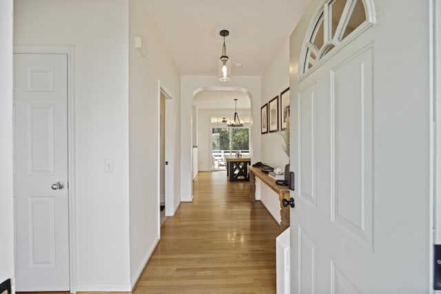 hallway featuring a chandelier, arched walkways, baseboards, and light wood-style floors