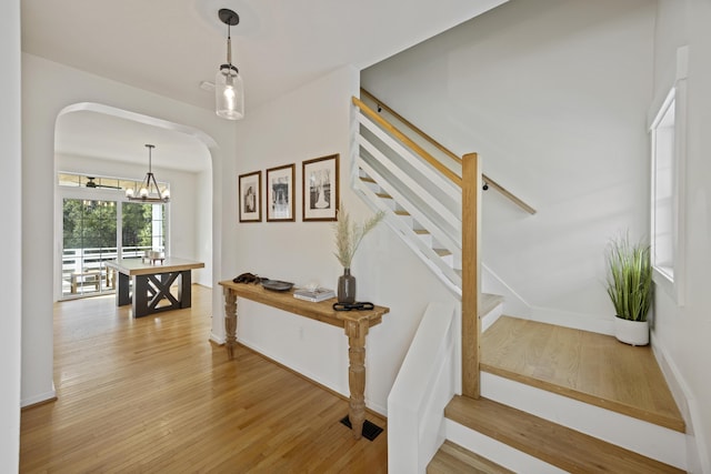 stairway featuring an inviting chandelier, wood finished floors, arched walkways, and baseboards