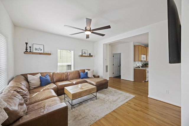 living area with visible vents, baseboards, light wood-style flooring, and a ceiling fan